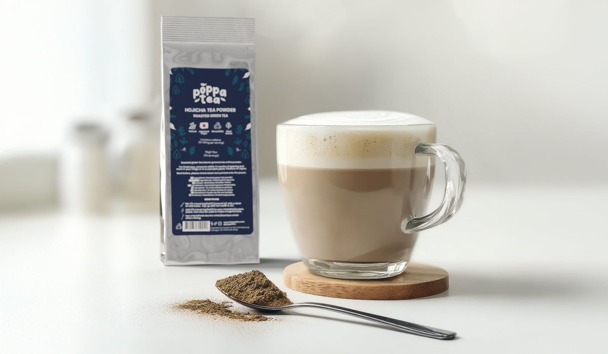 hojicha latte in a clear cup with a lovely milk froth. Roasted green tea powder on a spoon next to the drink.