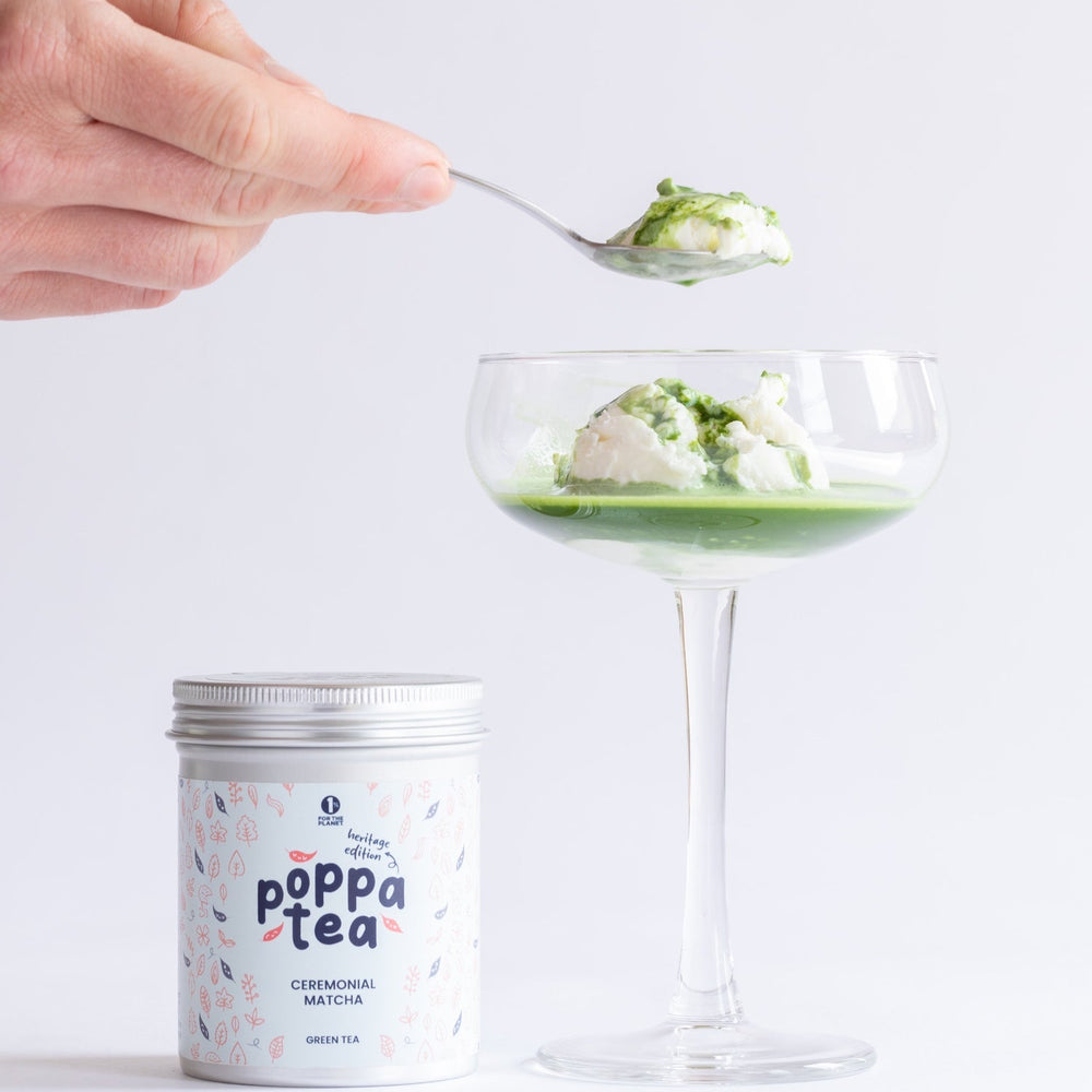 Hand holding a spoon over a glass with a matcha affogato dessert, next to a canister labeled 'Poppa Tea' on a light background
