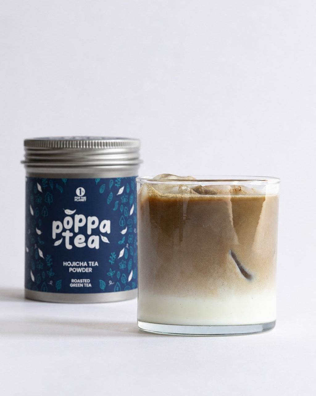 A silver canister of PoppaTea hojicha tea Powder with a dark blue label stands next to a glass of iced hojicha with milk on a clean white background.