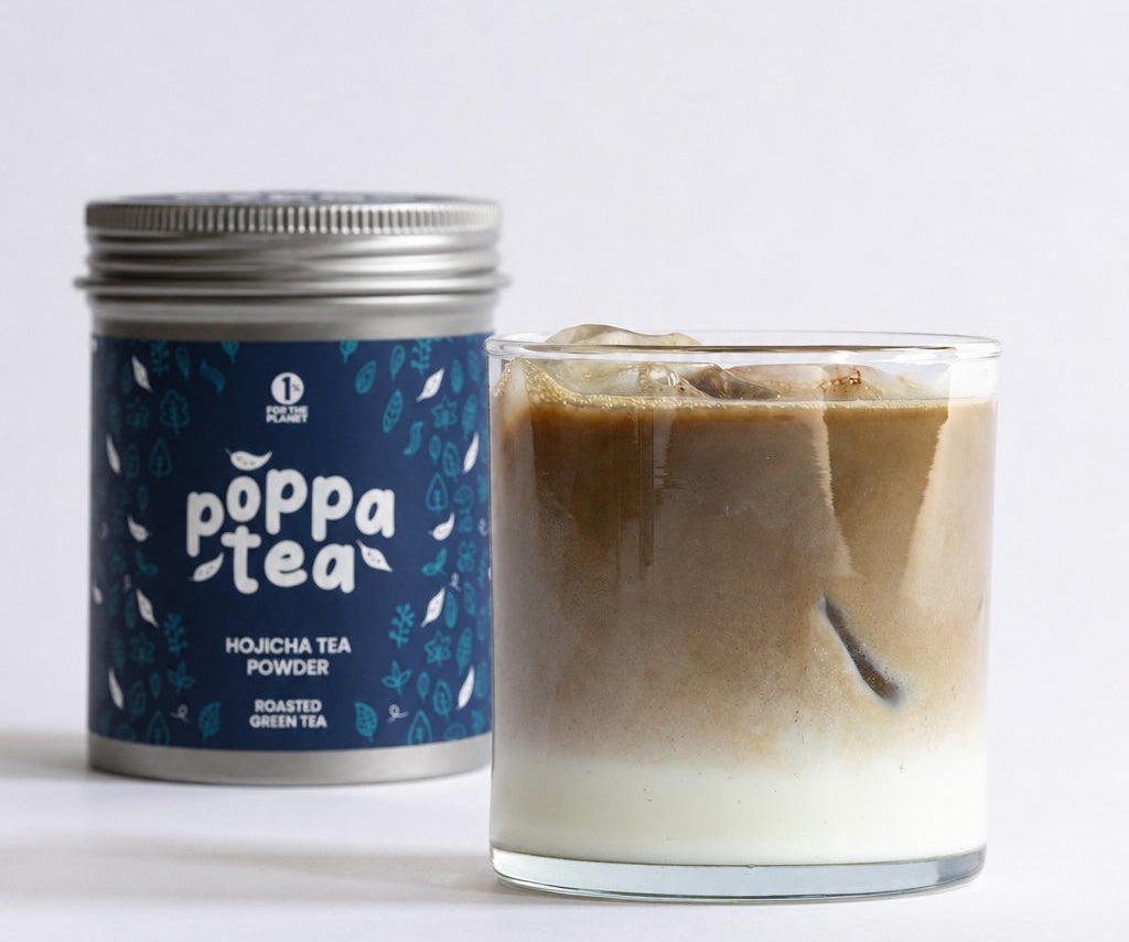 A silver canister of Poppa Tea hojicha Powder with a dark blue label stands next to a glass of iced coffee with milk on a clean white background.