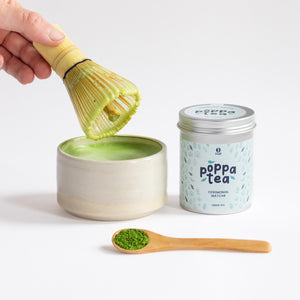 hot matcha latte in a traditional matcha bowl. Loose matcha powder on a spoon next to the hot drink.