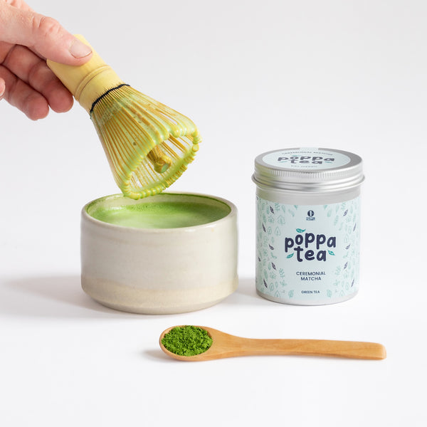 hot matcha latte in a traditional matcha bowl. Loose matcha powder on a spoon next to the hot drink.