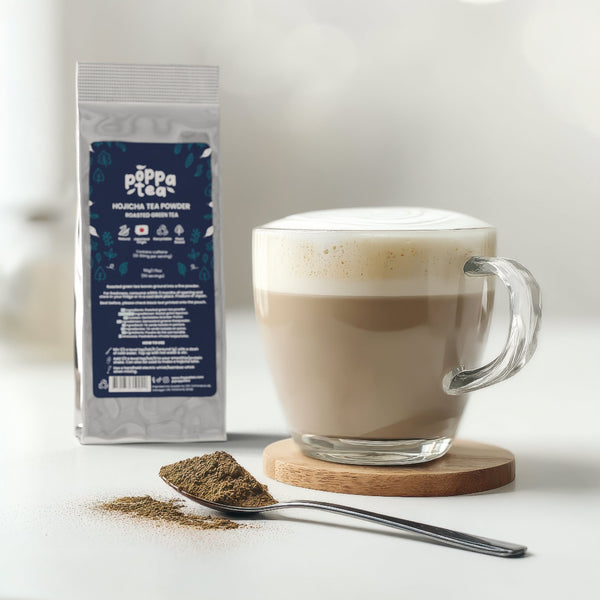 hot hojicha latte in a clear cup with loose roasted green tea powder and PoppaTea hojicha in the background