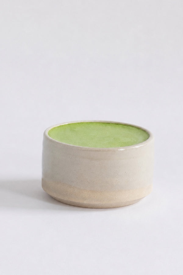 A small handmade ceramic bowl with a light beige exterior and a bright green glazed interior, photographed on a clean white background.