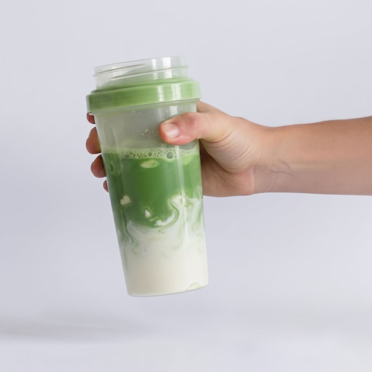 A hand holding a clear plastic shaker bottle with a green lid and green-and-white marbled contents, photographed against a clean light gray background.