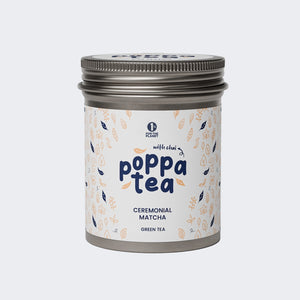 A tin container of Poppatea Ceremonial Matcha Green Tea with Chai, featuring a white label with floral and tea leaf illustrations.