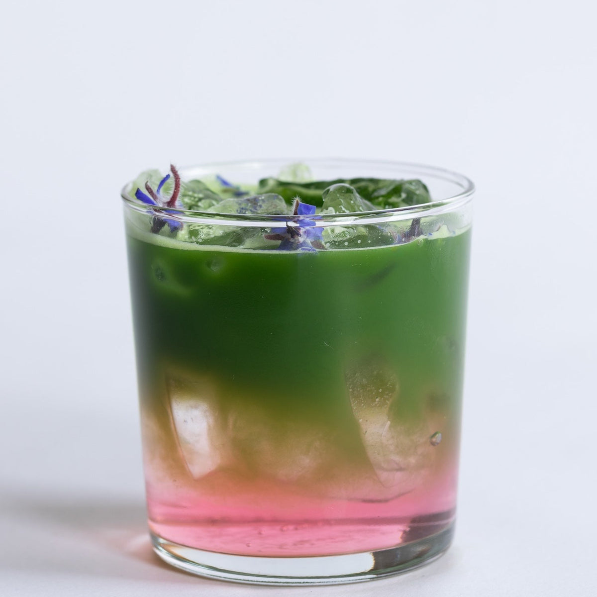Glass with a layered matcha green tea and pink drink on a white background