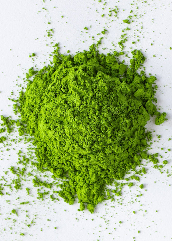 A pile of bright green matcha powder, displayed on a clean white background with scattered particles.