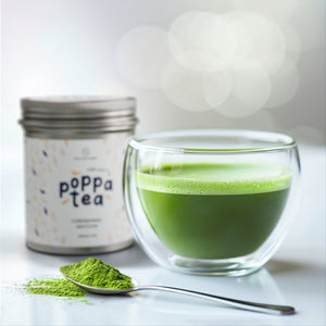 Image of traditional matcha tea in a clear glass jar and with a spoon of matcha tea with chai next to the cup